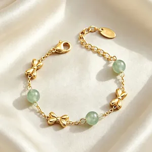 Close-up detail of golden bow-tie charms and green gemstone beads on a delicate chain