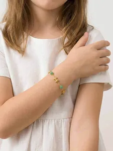 Detailed view of child's gold-plated stainless steel bracelet with bow-tie charms and green beads