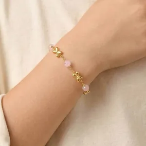 Close-up detail of a golden stainless steel bracelet with pink stone beads and bows