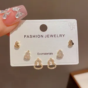 Close-up detail of three pairs of dainty gold gourd stud earrings set with sparkling crystals