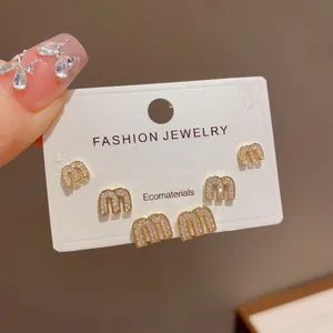 Close-up of "m" shaped gold stud earrings with rhinestones on a display card.