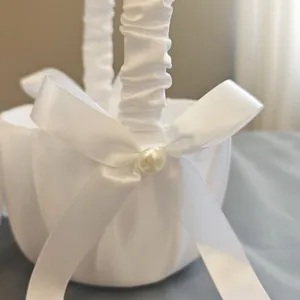 Macro view of white satin flower girl basket featuring elegant bow and pearl accent