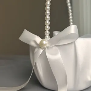 Elegant close-up of a white satin flower girl basket with pearl handle and ribbon bow