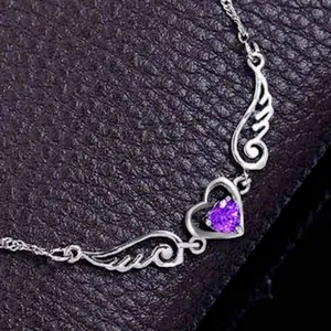 Detailed close-up view of silver angel wings necklace with a heart-shaped purple gemstone