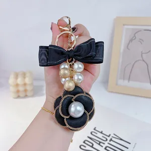 Elegant black camellia flower keychain with white pearls and a double bow detail