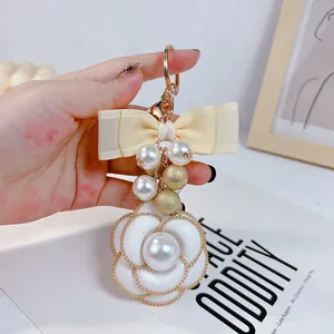 Close-up detail of camellia flower keychain with elegant cream ribbon bow and pearls