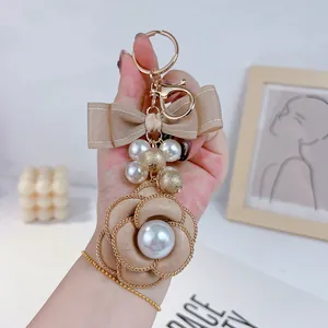 Elegant camellia keychain with pearls and a double-layered beige ribbon bow detail.