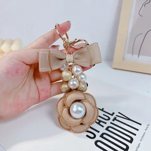 Elegant beige camellia bag charm featuring double-layered bow and lustrous pearl beads