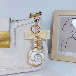 Detailed view of white camellia bag charm featuring pearls and a yellow ribbon bow