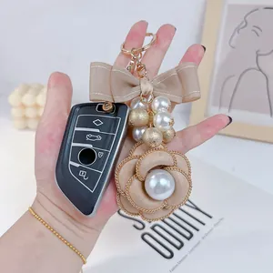 Close-up of elegant camellia pearl keychain with a tan bow accessory held in hand