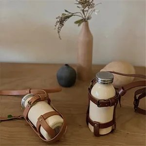 Close-up of a rustic brown leather coffee cup sleeve with an adjustable shoulder strap