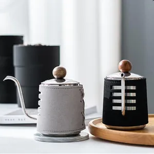 Detail view of small pour over kettles with grey and black leather sleeves on wooden tray