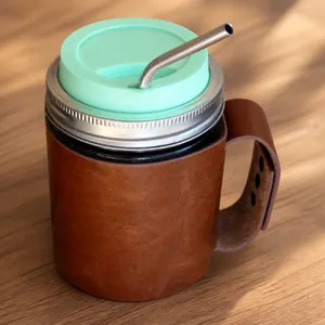 Λεπτομέρεια καφέ δερμάτινης θήκης για Mason jar με πράσινο καπάκι και μεταλλικό καλαμάκι.
