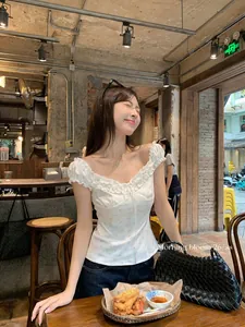 Model wearing a white floral ruffle off-shoulder slim fit cropped top in a cafe