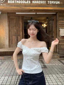 Close-up of a white floral off-the-shoulder top with wood-ear trim in a street setting