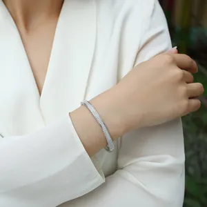 Detailed view of a silver moissanite bangle on a woman's wrist with pavé stones.