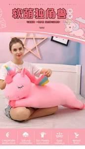 Young woman sitting on a cozy bed holding a giant soft pink unicorn plush toy as a gift