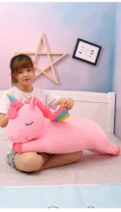Young woman sitting on a cozy bed holding a giant soft pink unicorn plush toy as a gift