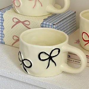 Charming cream ceramic mug with hand-painted black bow design and chunky handle style