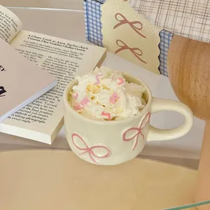 Elegant creamy white ceramic mug featuring pink bow relief design in aesthetic desk setting