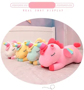 A row of four colorful unicorn plush toys in pink yellow and mint on a cozy white bed