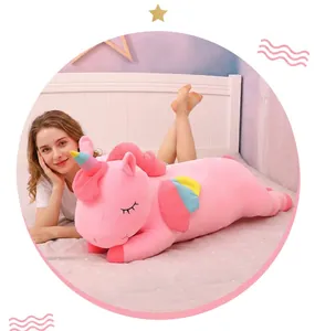 Close-up view of a large pink unicorn plush toy with rainbow wings on a cozy bed.