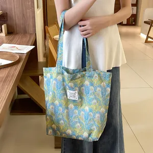 Sac cabas en toile à motif plumes de paon tenu par un mannequin dans un café élégant