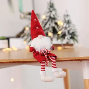 Detailed view of a red plush Christmas gnome doll sitting on a wooden table edge with bokeh lights.
