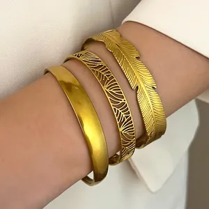 Close-up of stacked gold stainless steel bracelets with feather and filigree designs