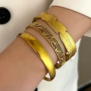 Detailed close-up of stacked bohemian gold feather and hollow stainless steel bracelets.