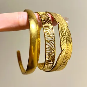 Detail of three stackable gold bracelets with plain, filigree, and feather designs