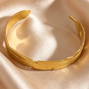 Macro detail of a vintage gold luxury feather-patterned stainless steel cuff bracelet.