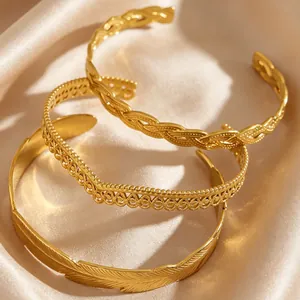 Close-up of stacked gold stainless steel bangles with feather and braided designs
