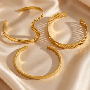 Detail view of gold-plated stainless steel cuff bracelets with geometric cutouts and textured finish.