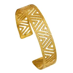 Close-up of vintage gold cuff bracelet with geometric hollow-out pattern and texture.