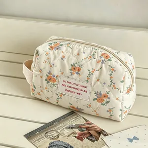 Detailed view of a cream-colored floral quilted makeup bag placed on a minimalist bench