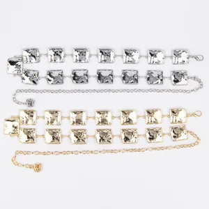 Close-up detail of two-color metal waist chains with square plates and floral charms.
