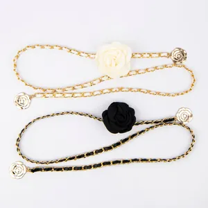 Close-up of elegant gold chain waist belts featuring white and black rose decorations.