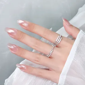Close-up of minimalist silver cross-knot and triple-band open rings with rhinestones