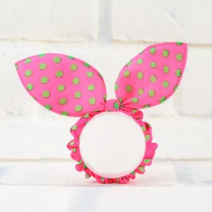 Close-up detail of a vibrant pink rabbit ear hair scrunchie with green polka dot pattern