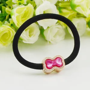 Close-up of black elastic hair tie with a cute pink bow-shaped charm and gold border.