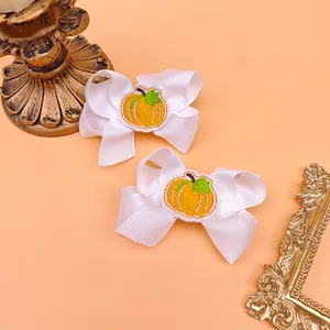 Close-up detail of white ribbon bow hair clips with cute pumpkin embroidery for kids.