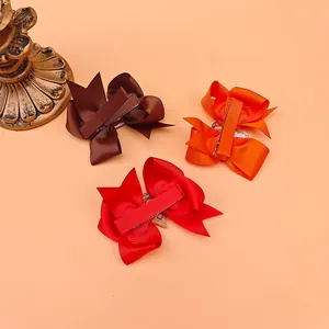 Detail of three grosgrain ribbon bow hair clips in brown, orange, and red colors.