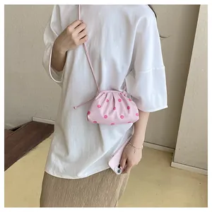 Close-up of a stylish pink pleated dumpling bag with red polka dots worn by a model