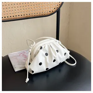 Detailed view of a white pleated dumpling bag with black polka dots placed on a chair