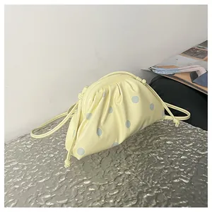 Detail of a pleated yellow dumpling bag with blue polka dots and a slim strap.