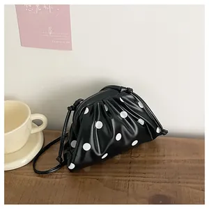 Close-up detail of a pleated black dumpling bag with white polka dots in a cozy room