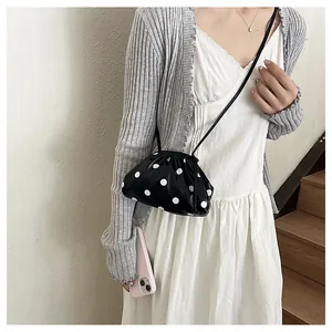Detail of black and white polka dot pleated dumpling bag worn as a crossbody.
