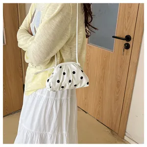 Fashionable white ruched dumpling bag with black polka dots worn as a shoulder bag by a woman