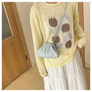 Detail shot of a light blue polka dot pleated cloud bag worn with a yellow knitted sweater